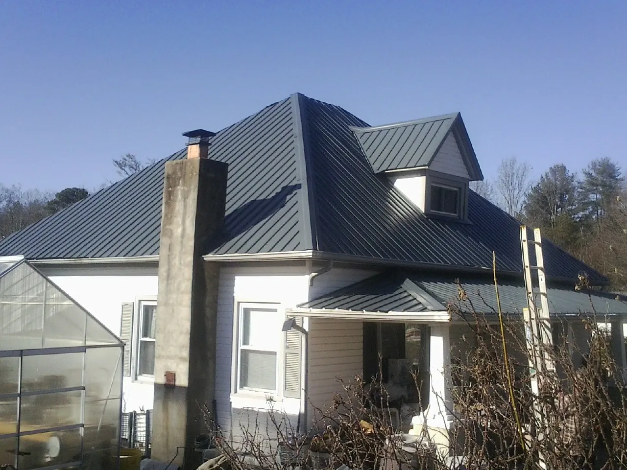 Dark blue standing seam metal roof on a white farmhouse with dormer — Slate & Tile Roof Repair by Roofing Brothers in Prospect Heights