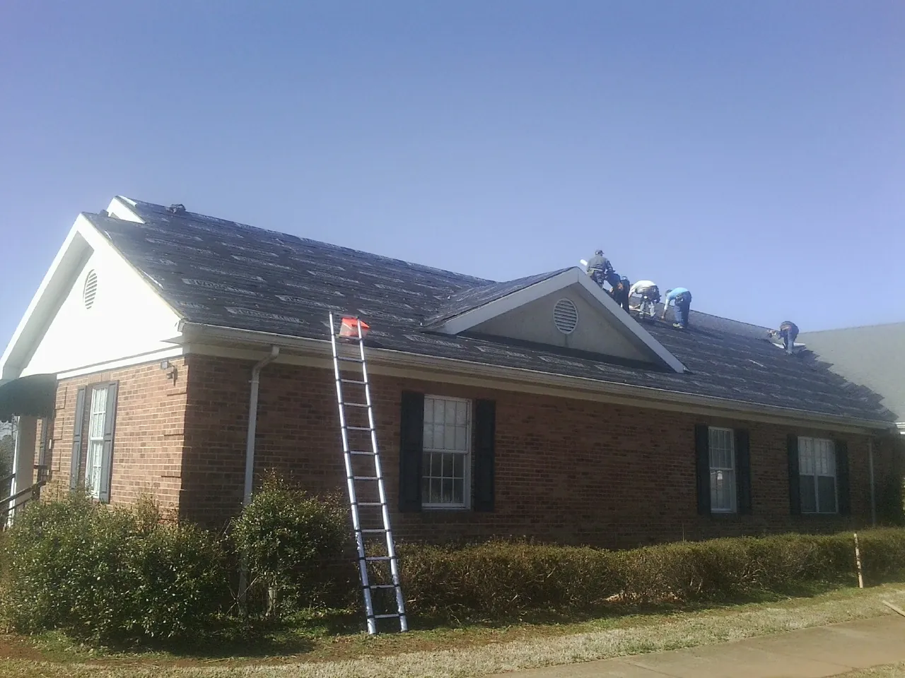 Crew tearing shingles off a brick ranch roof with a ladder set — Emergency Roof Repair work by our crew in Prospect Heights