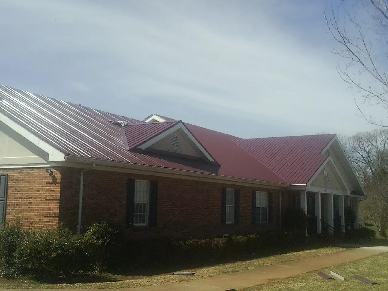 Red metal roof with gabled entries on a long brick building, from a Hail Damage Roof Repair job in Prospect Heights
