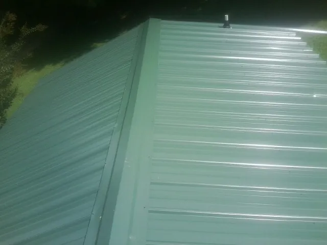 New green metal panels meeting at the ridge of a roof — Flat Roof Repair work by our crew in Prospect Heights