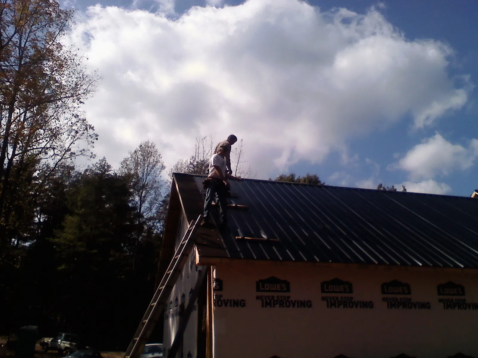 Roofer fastening dark metal panels high against a cloudy sky, from a Roof Inspection job in Prospect Heights