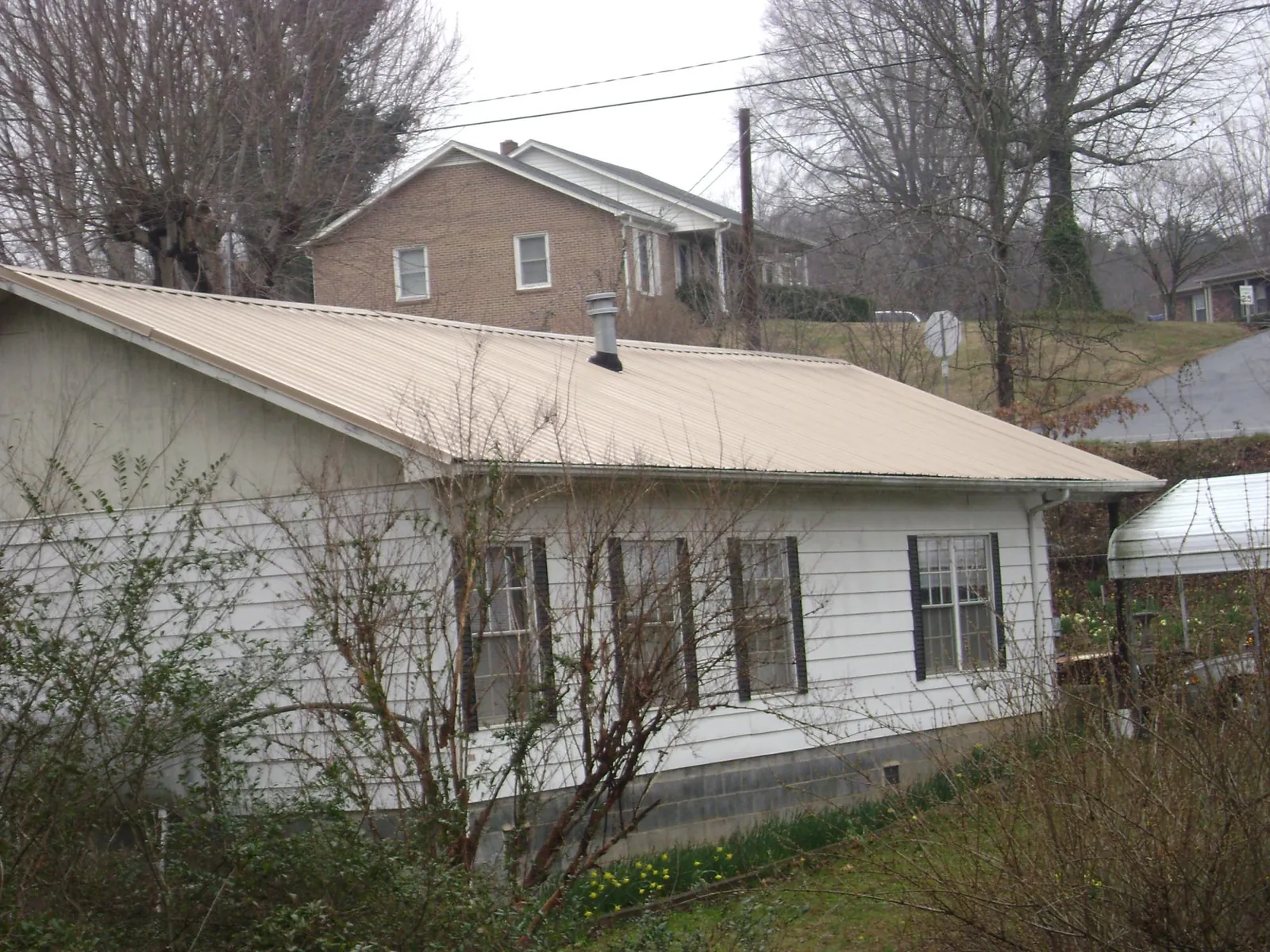 Tan metal roof on a white sided house set into a hillside — Commercial Roofing by Roofing Brothers in Prospect Heights