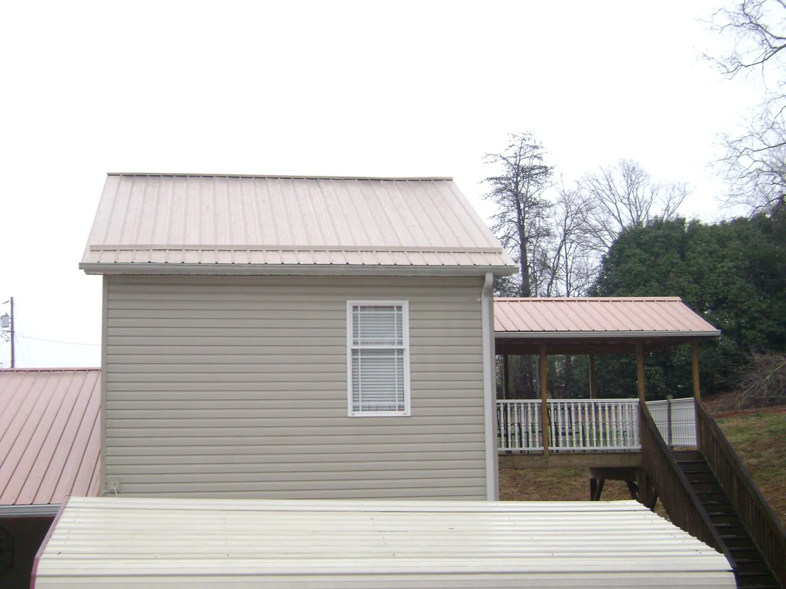 Tan metal roofs on a two story addition and attached porch, from a Roof Replacement job in Prospect Heights